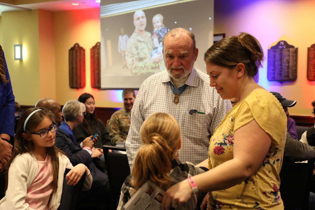 A man with a medal around his neck talks to a child and a person.