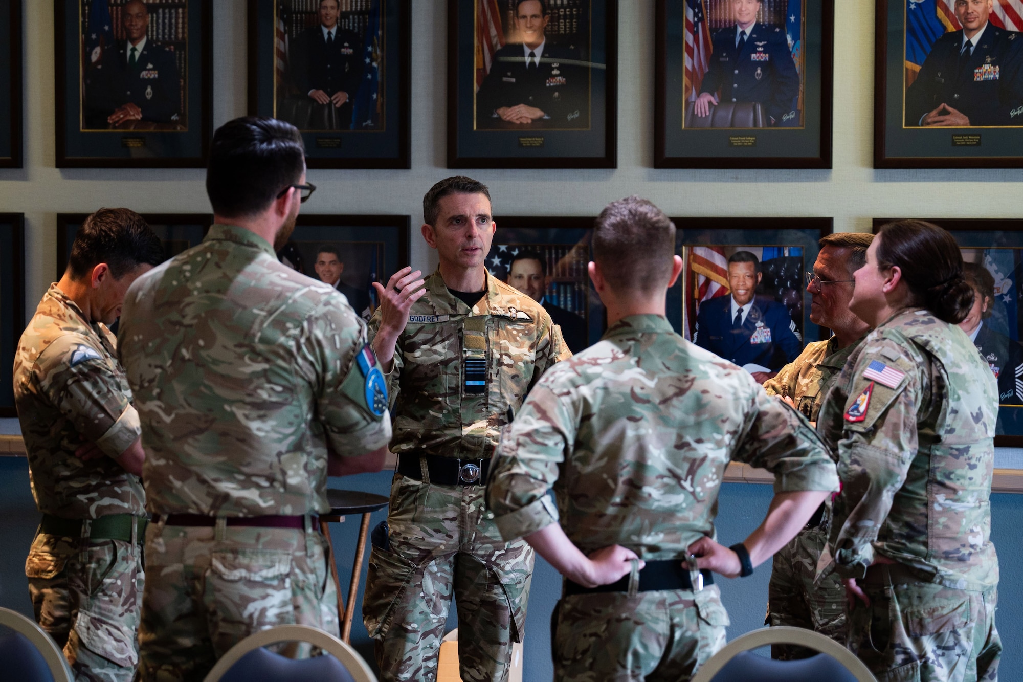 Six military members discuss topics in a circle inside of a room with portraits hanging on the wall.