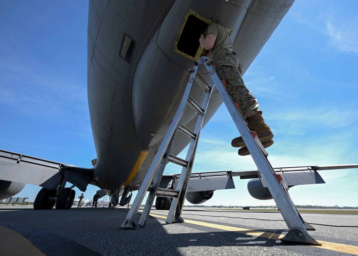 A man in a military uniform stands on a ladder and works on a military plane.