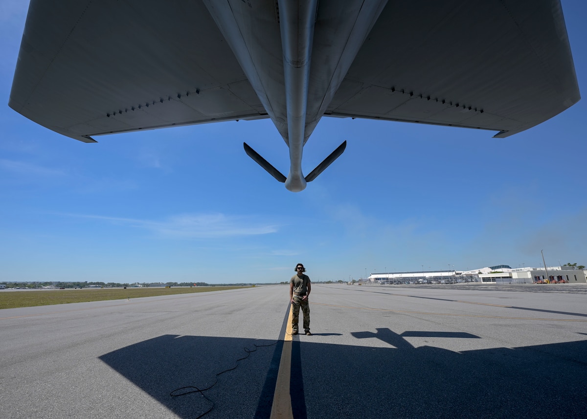 A man in a military uniforms stands below a military plane.