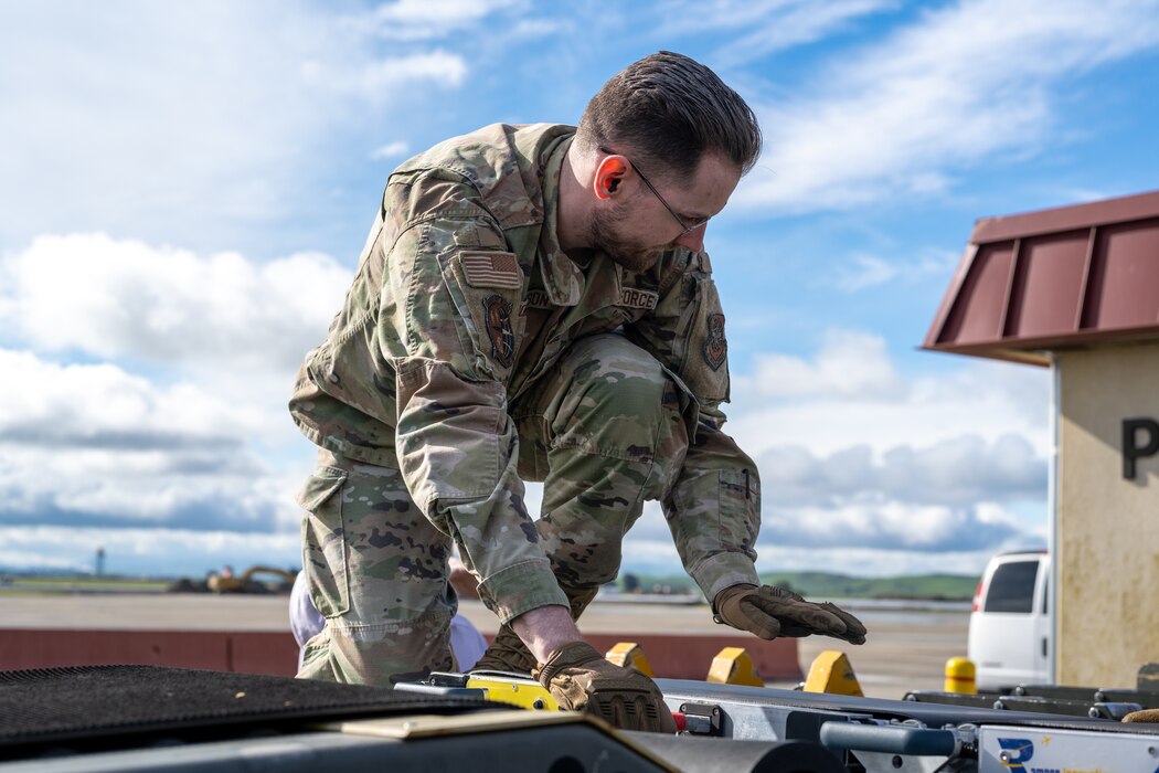 An Airman attaches power cables to a conveyer system on the flight line
