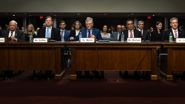 Four men in business attire sit alongside each other at a series of desks.