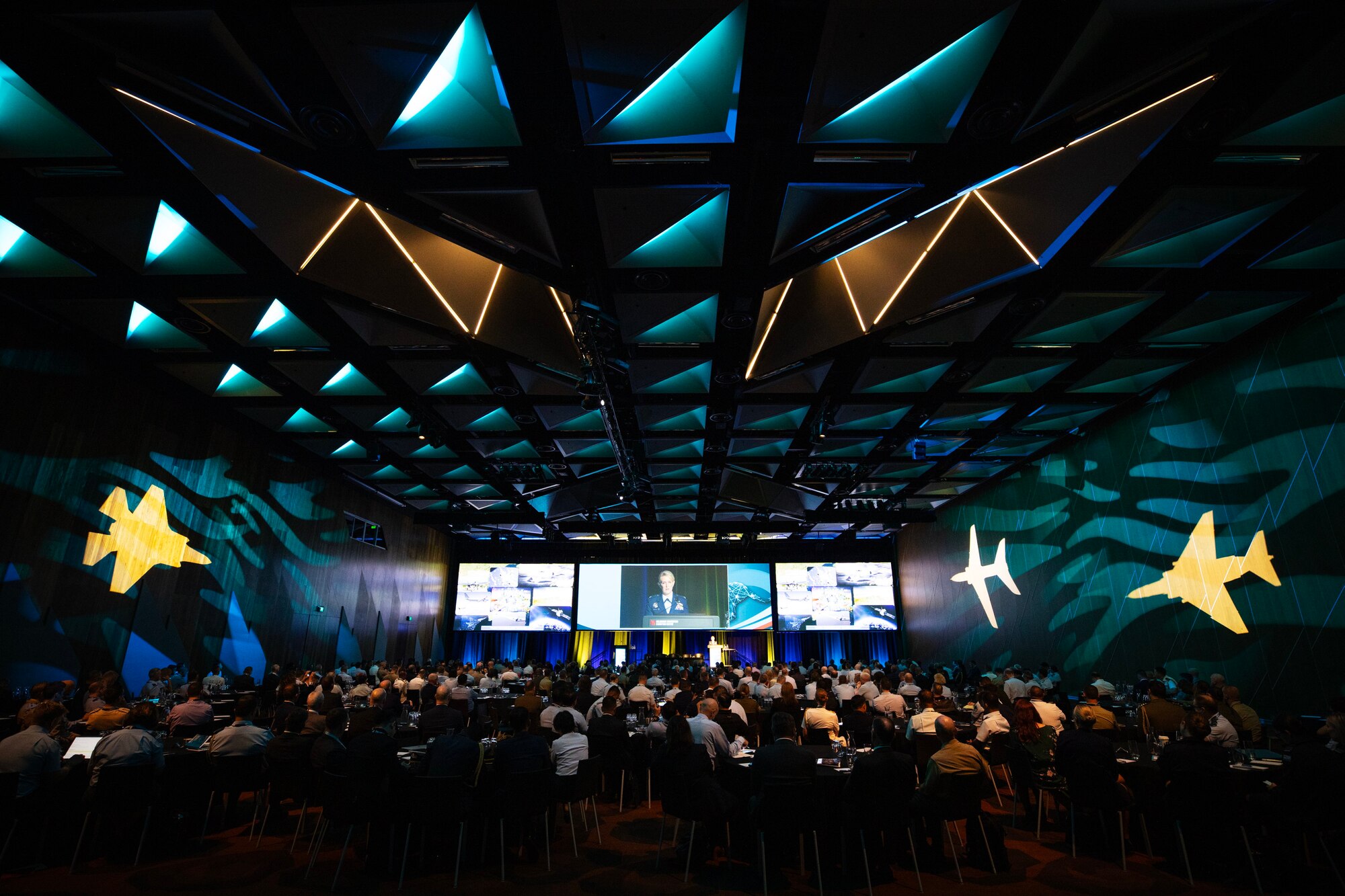 A Large room with an audience facing a distant stage.