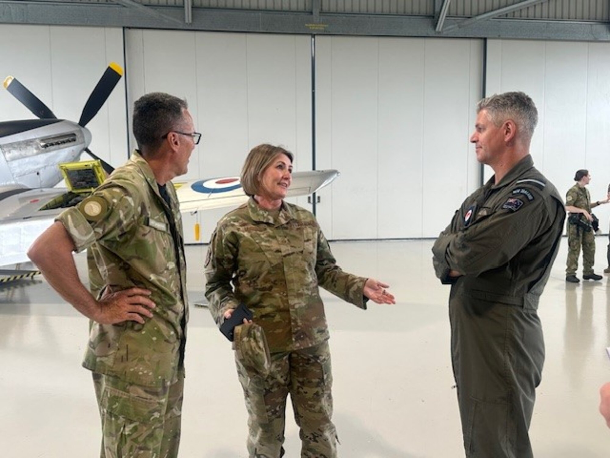 Three people chat in a hangar