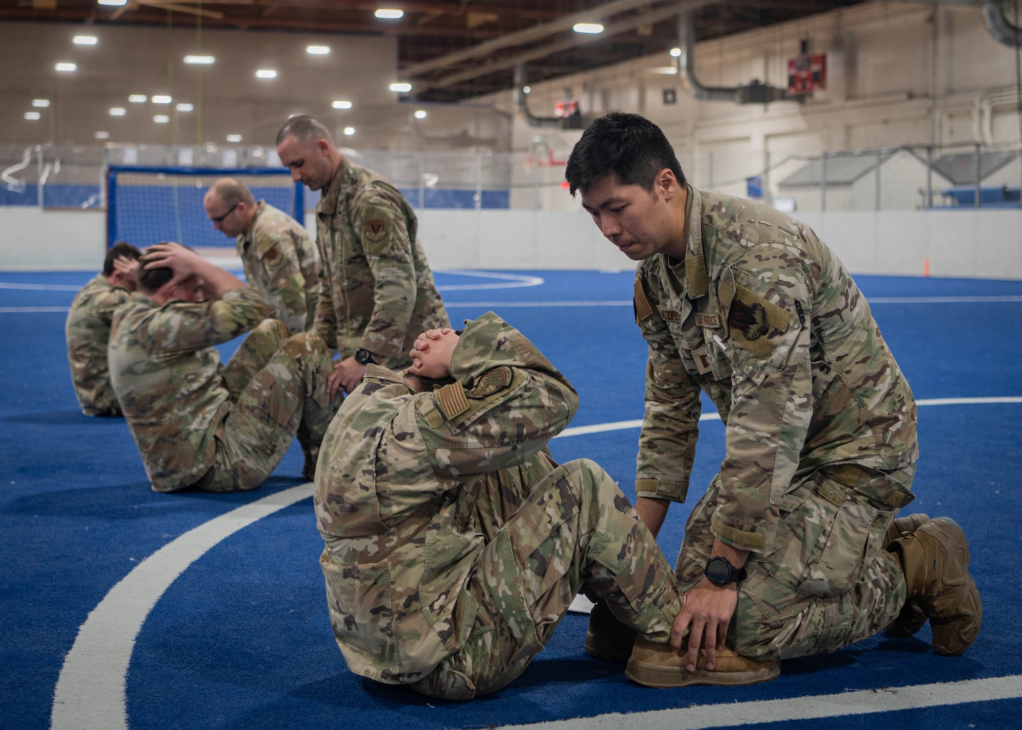 Service members are evaluated on their sit ups during the physical fitness portion of Savage Raider Team tryouts at the Offutt Field House gym March 4, 2025. To qualify and advance, each recruit had to complete pushups, sit ups, pull ups, a weighted run and buddy drag. (U.S. Air Force photo by Daniel Martinez)