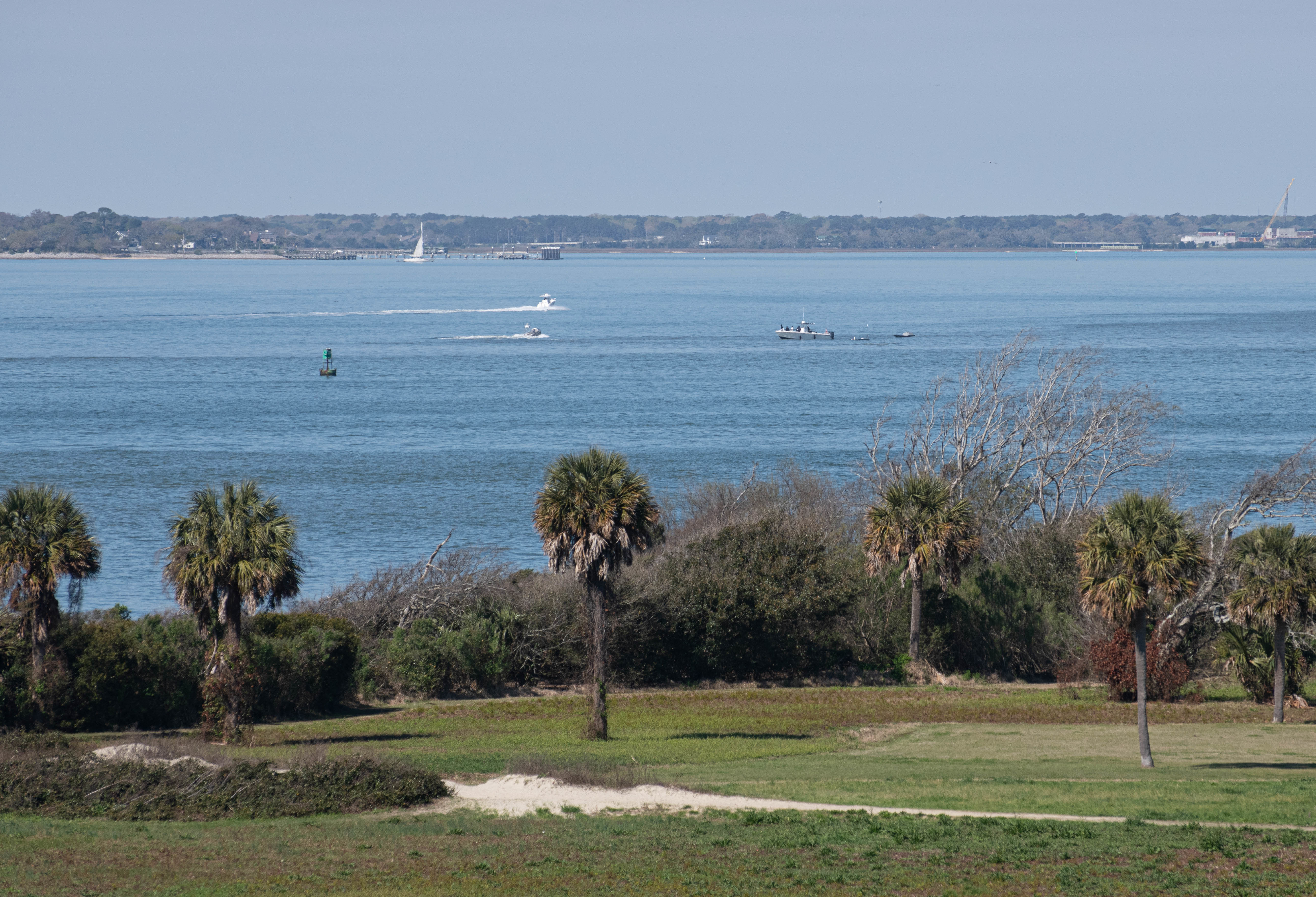 Photo overview of Sullivan's Island with palmetto trees and Charleston bay in the background with naval assets.