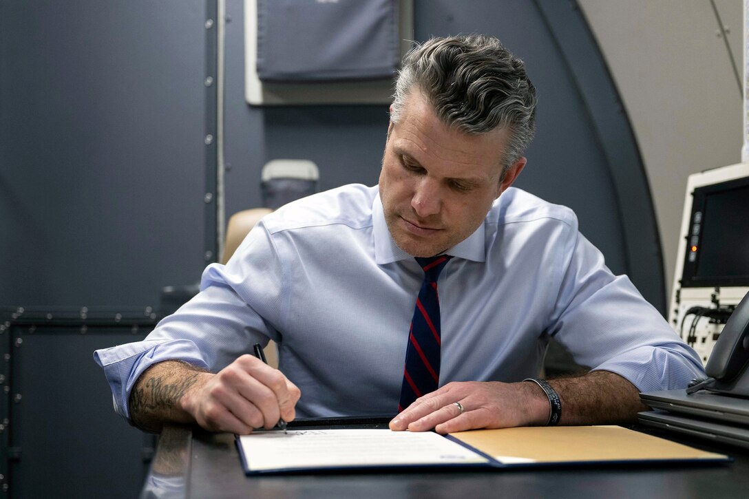 A man wearing a shirt and tie signs on a paper while sitting down aboard an aircraft.