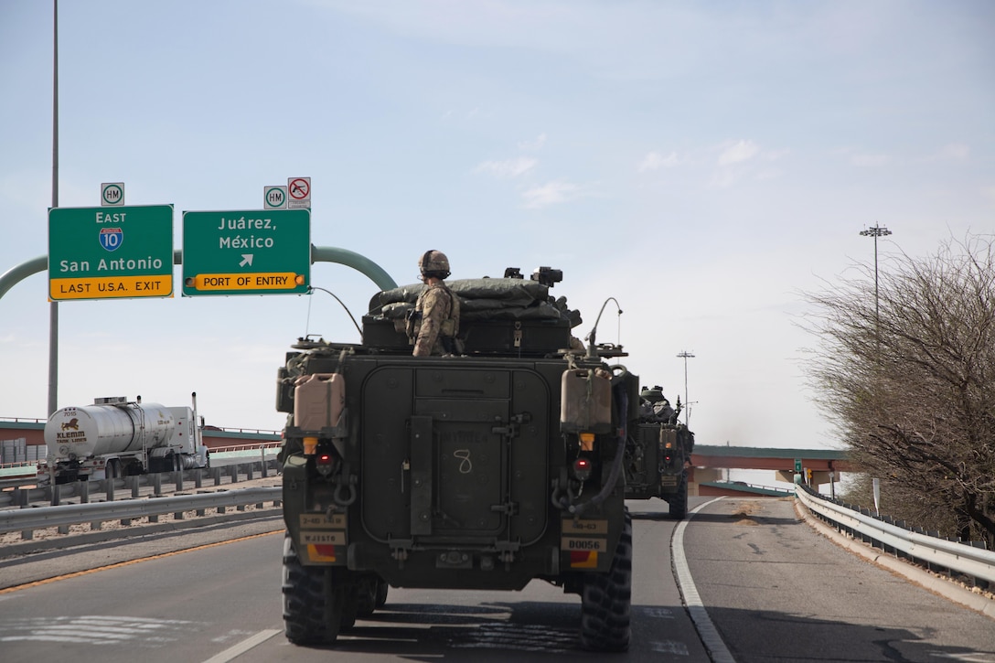 Soldiers drive two armored military vehicles on a highway.
