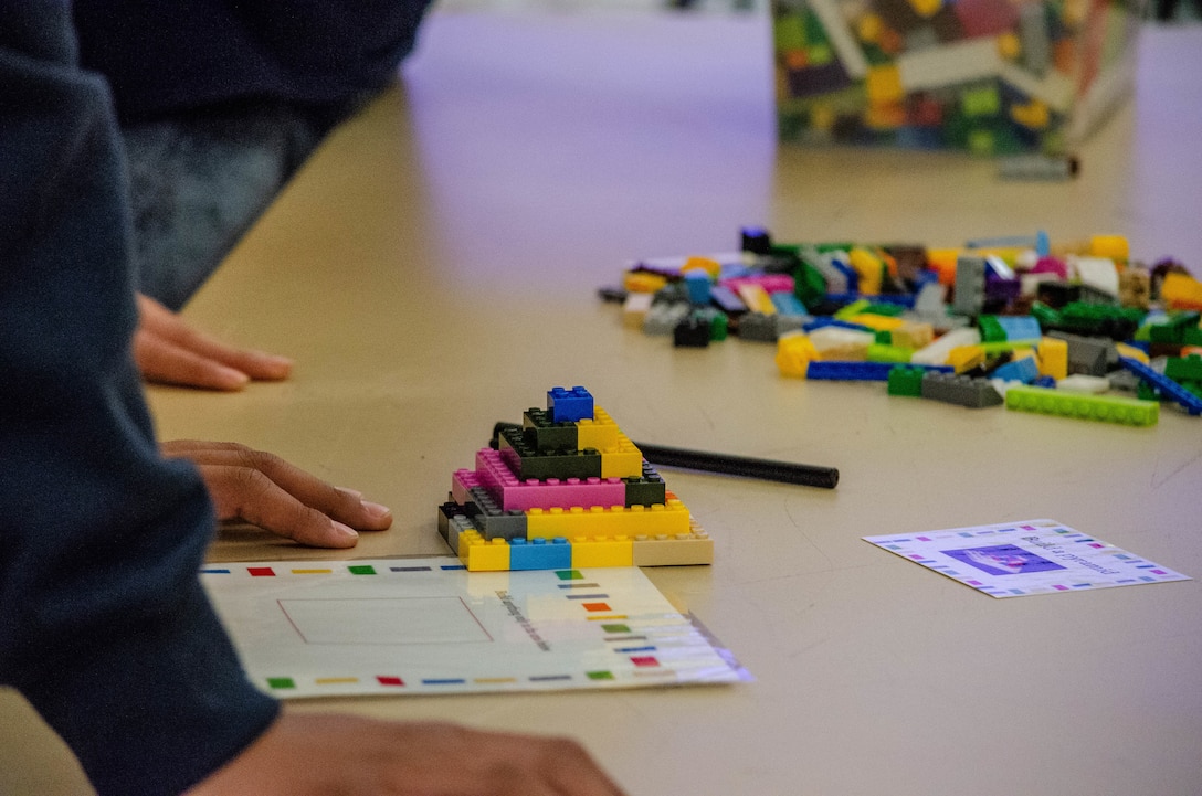 a pyramid of multicolored building blocks sit on a table with loose building block pieces in the distance.