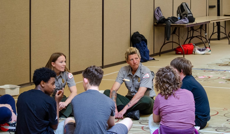 Two USACE Sacramento District park rangers sit cross-legged on the ground with group of middle schools students