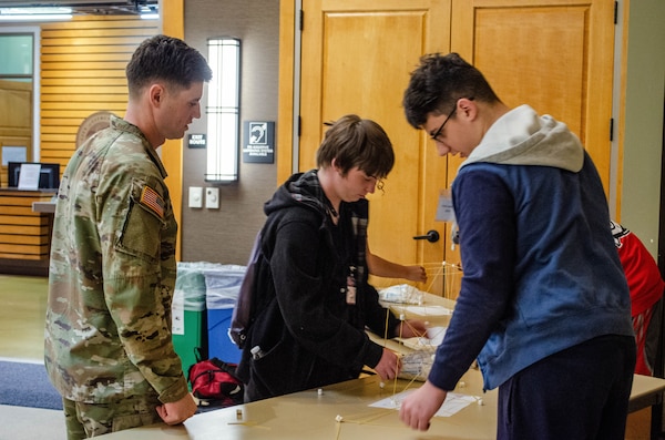 Two students construct a tower using uncooked spaghetti noodles and marshmallows while USACE Sacramento project engineer Lt. Matthew Sauter watches.