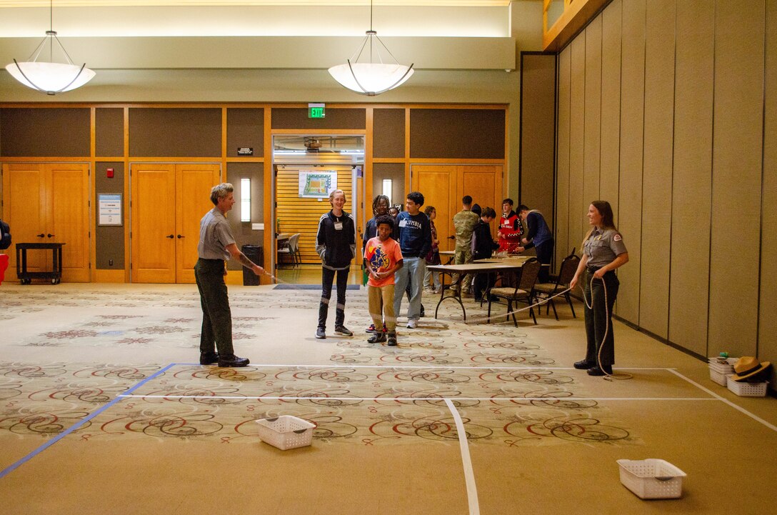 children line up to jump over a jump rope being held by two USACE Sacramento District park rangers as part of a game to demonstrate how salmon migrate upstream.