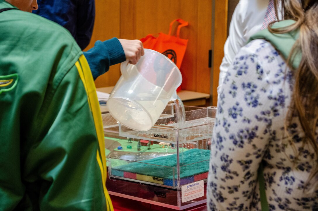 water flows from clear bucket into flood model table while students look on.
