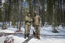Two men in military uniform stand shoulder to shoulder in center frame.
