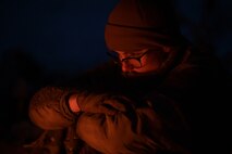 A person's face is slightly illuminated in an orange flow from a campfire in front of them.