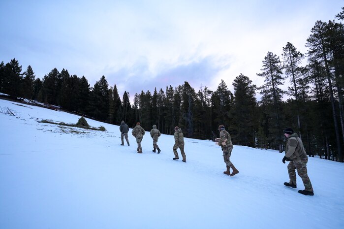 Eight people in military uniform hike uphill in the snow.