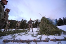 A group of people observe a pyre of tree boughs as it begins to smoke.