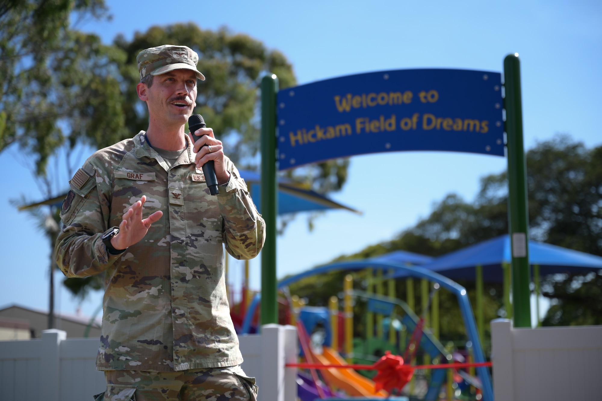 An Airmen speaks in front of a playground.