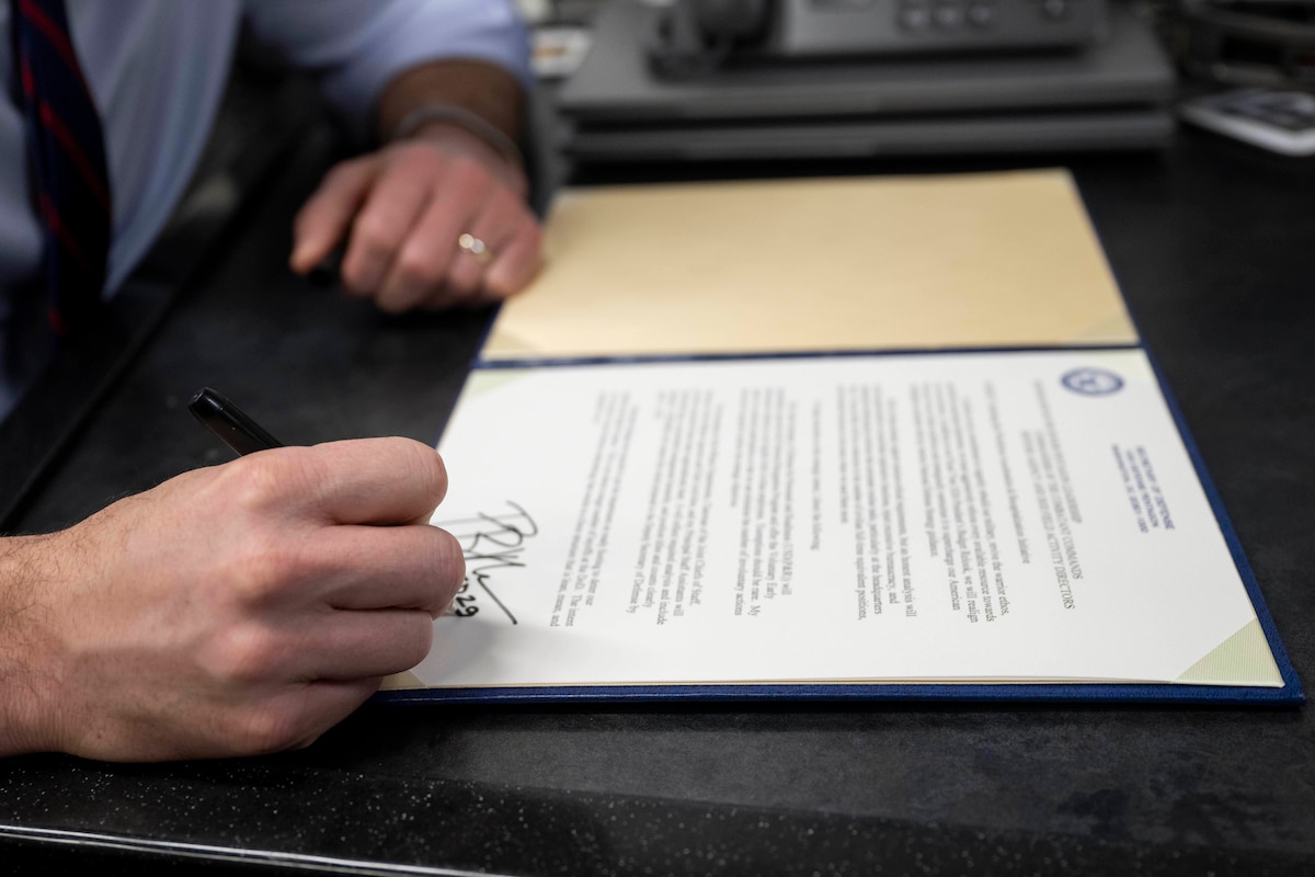 A hand holding a pen is signing a document on a desk.
