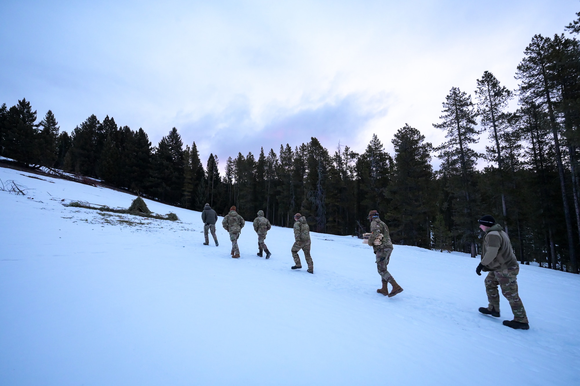 Eight people in military uniform hike uphill in the snow.