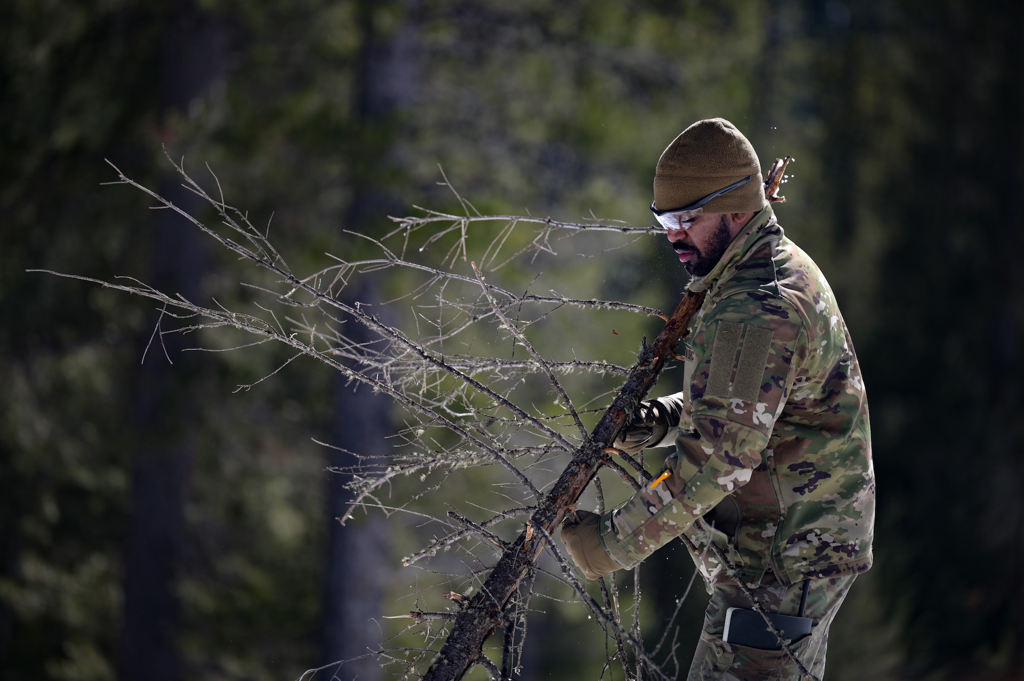 A man in military uniform removes branches from a dead tree branch.