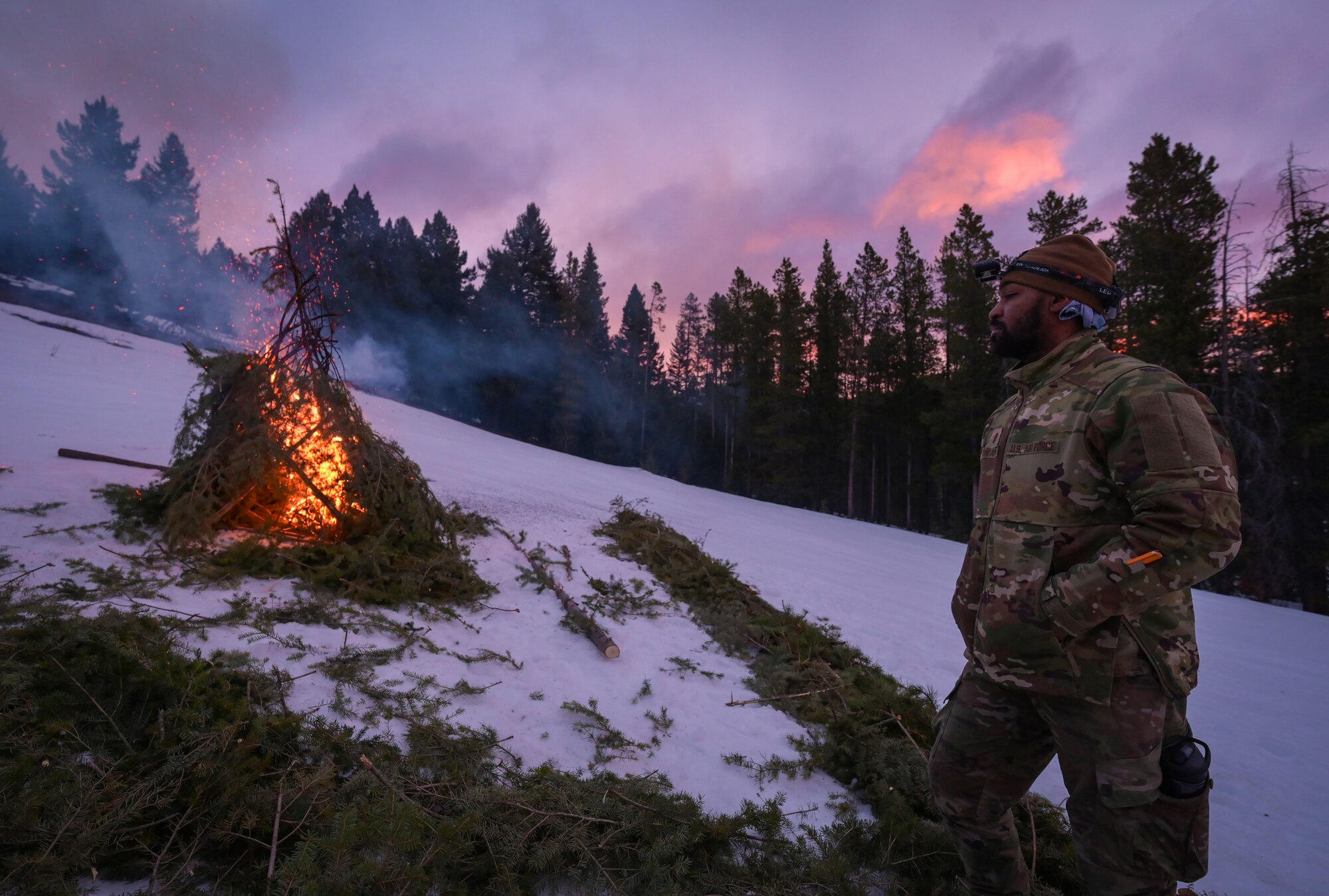 A man in military uniform stands to observe a burning pyre.