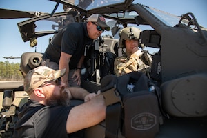 Two men engineers review the instrument panel of an Apache helicopter with the pilot.