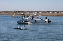 A boat in the water with unmanned autonomous vehicle operators overseeing two unmanned autonomous vehicles.