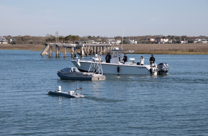 A boat in the water with unmanned autonomous vehicle operators overseeing two unmanned autonomous vehicles.