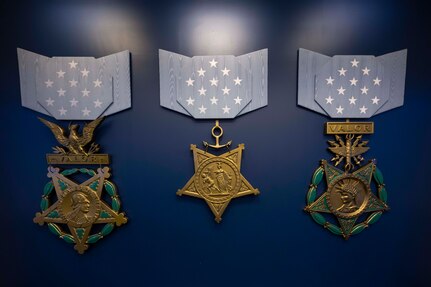 Three medals attached to blue ribbons rest on a dark blue background.