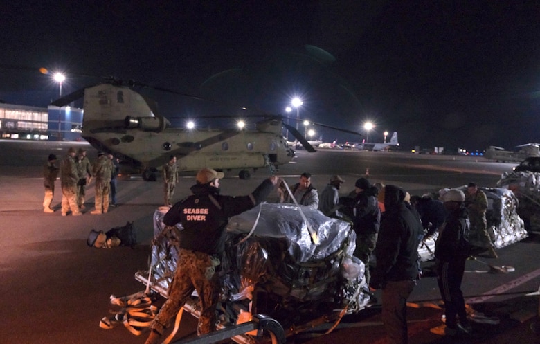 Members of Commader, Task Force (CTF) 68 U.S. navy dive team work with flight crews late into the night to load diving equipment from a U.S. Air Force C-130 Hercules aircraft to a CH-47 Chinook flown by U.S. Army soldiers apart of  2nd Battalion, 501st Aviation Regiment, 1st Combat Aviation Brigade, 1st Armored Division, be used in the ongoing efforts to recover four U.S. soldiers in a submerged M88 Hercules on a training site near Pabadre, Lithuania on March 29, 2025.