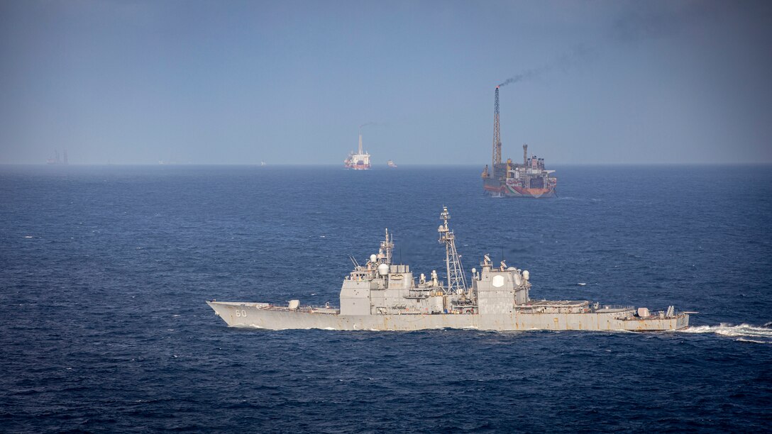 U.S. Navy Ticonderoga-class guided-missile cruiser USS Normandy (CG 60) passes floating production, storage, and offloading (FPSO) vessels supporting Guyana's energy development in the Stabroek Block off the coast of Guyana in the North Atlantic Ocean, March 27, 2025. Normandy is scheduled to protect U.S. interests in the region and strengthen maritime partnerships through bilateral and multinational maritime operations and Theater Security Cooperation (TSC) port visits. U.S. Naval Forces Southern Command/U.S. 4th Fleet is the maritime component of U.S. Southern Command and the trusted maritime partner for Caribbean, Central, and South American maritime forces leading to improved unity, security, and stability. (U.S. Navy photo by Mass Communication Specialist 2nd Class Dylan M. Kinee/Released)