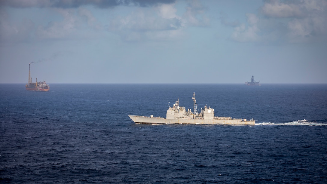 U.S. Navy Ticonderoga-class guided-missile cruiser USS Normandy (CG 60) passes floating production, storage, and offloading (FPSO) vessels supporting Guyana's energy development in the Stabroek Block off the coast of Guyana in the North Atlantic Ocean, March 27, 2025. Normandy is scheduled to protect U.S. interests in the region and strengthen maritime partnerships through bilateral and multinational maritime operations and Theater Security Cooperation (TSC) port visits. U.S. Naval Forces Southern Command/U.S. 4th Fleet is the maritime component of U.S. Southern Command and the trusted maritime partner for Caribbean, Central, and South American maritime forces leading to improved unity, security, and stability. (U.S. Navy photo by Mass Communication Specialist 2nd Class Dylan M. Kinee/Released)