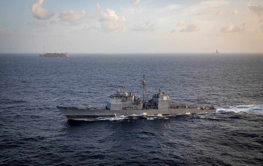 U.S. Navy Ticonderoga-class guided-missile cruiser USS Normandy (CG 60) passes floating production, storage, and offloading (FPSO) vessels supporting Guyana's energy development in the Stabroek Block off the coast of Guyana in the North Atlantic Ocean, March 27, 2025. Normandy is scheduled to protect U.S. interests in the region and strengthen maritime partnerships through bilateral and multinational maritime operations and Theater Security Cooperation (TSC) port visits. U.S. Naval Forces Southern Command/U.S. 4th Fleet is the maritime component of U.S. Southern Command and the trusted maritime partner for Caribbean, Central, and South American maritime forces leading to improved unity, security, and stability. (U.S. Navy photo by Mass Communication Specialist 2nd Class Dylan M. Kinee/Released)