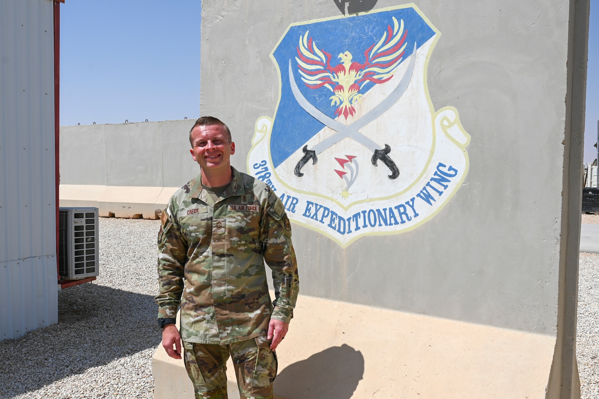 U.S. Air Force Chief Master Sgt. Steven Creek, 378th Air Expeditionary Wing command chief, poses in front of a mural of the wing patch in the U.S. Central Command area of responsibility, March 18, 2024.