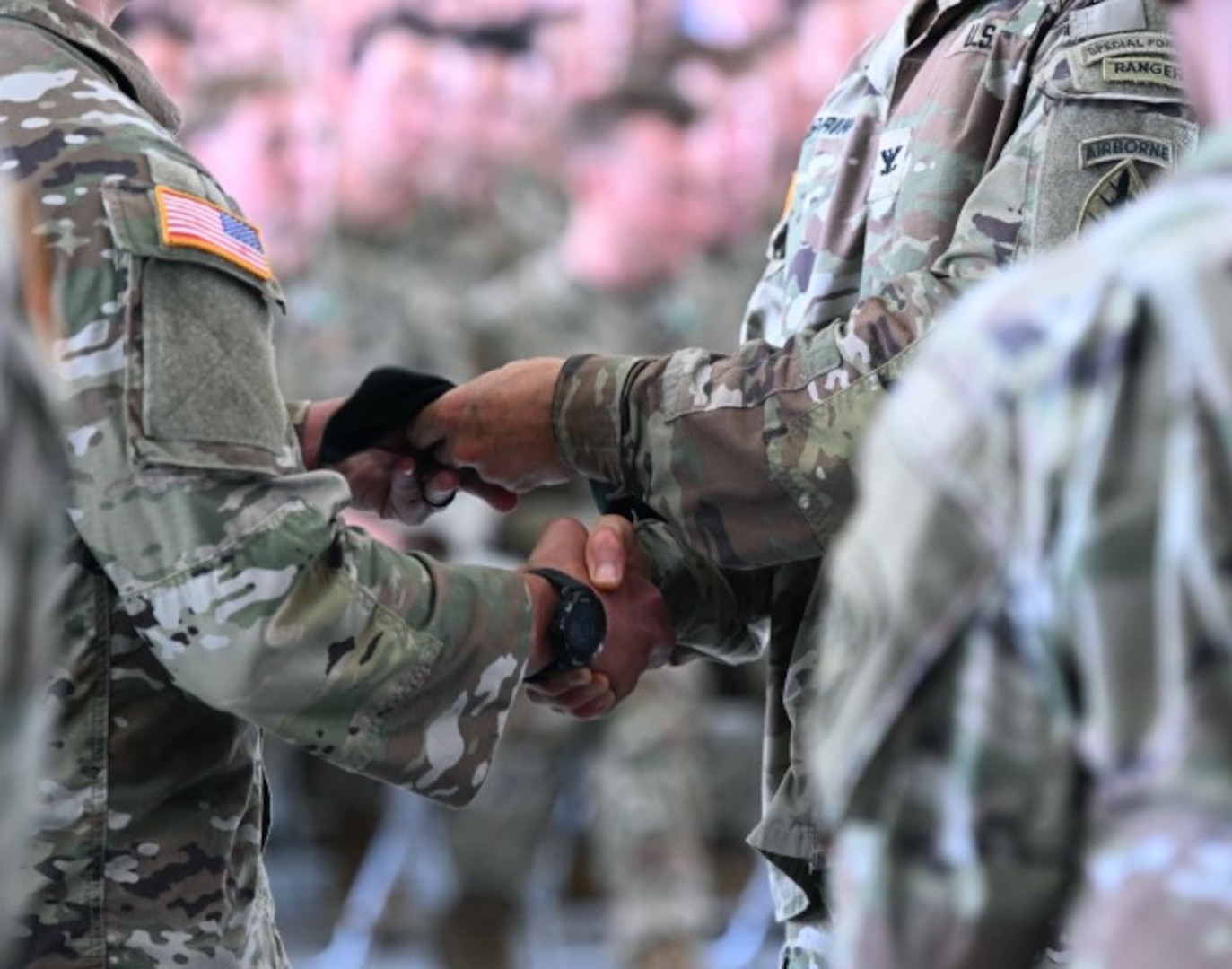 Two men dressed in military attire exchange a beret in front of a crowd.