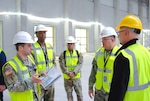 Five people wearing reflective safety vests and hard hats stand in an indoor construction area having a discussion.