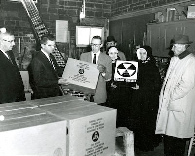 Black and white image of a group of men and women standing with boxes.