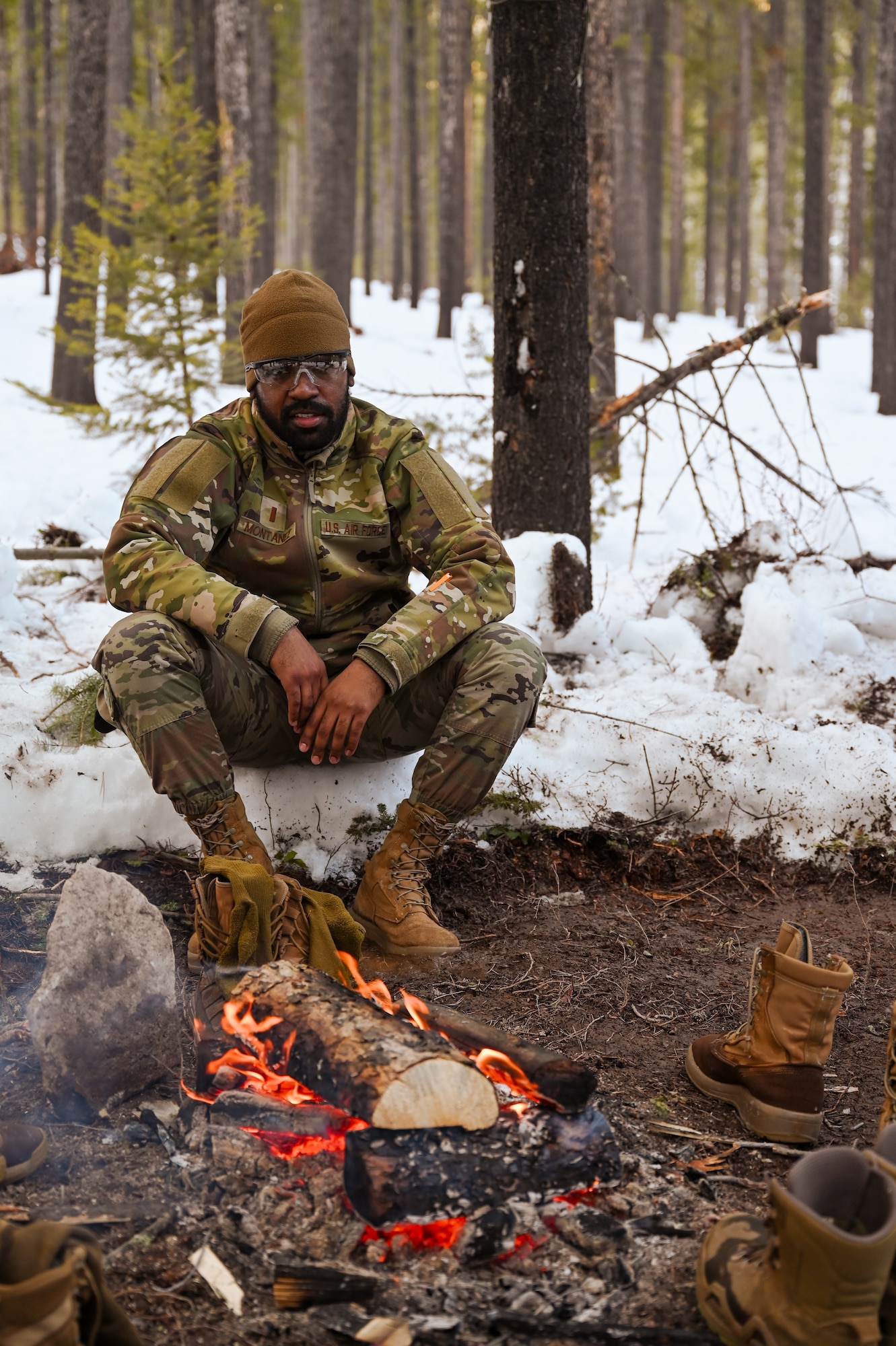 Airman sits in snow next to a fire in the woods
