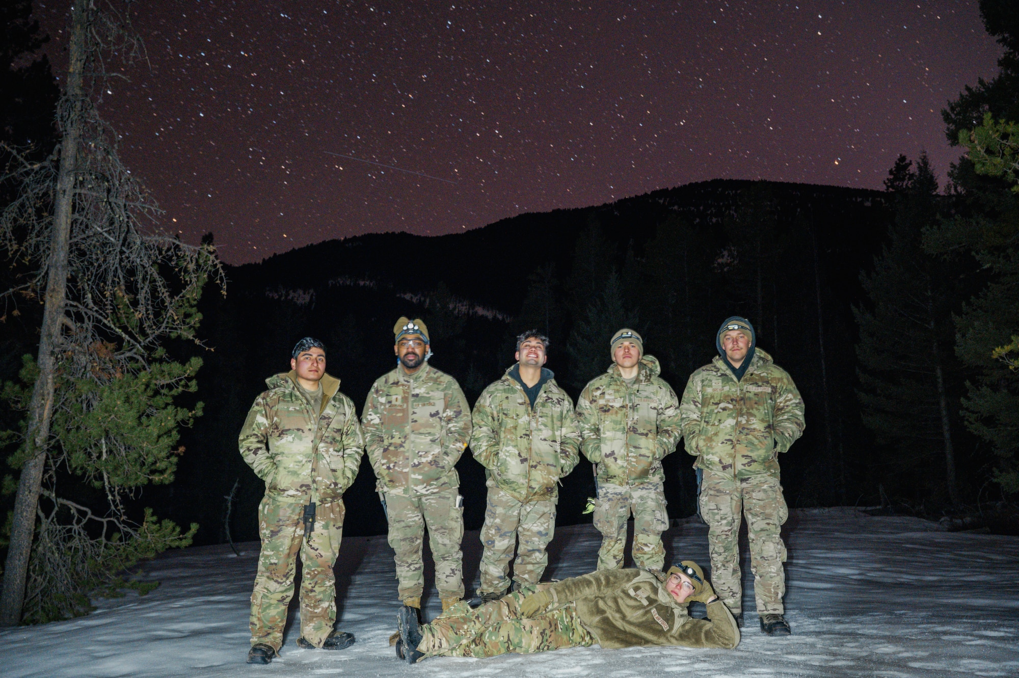Airmen pose for a photo in the dark with stars in the background in the woods