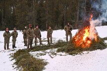 Airmen in uniform in the woods standing next to fire