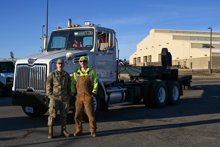 Two Airmen pose in front of a forty-foot tractor truck.