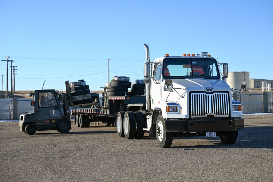 A forklift loads pallets of tires onto a forty-foot flatbed truck.