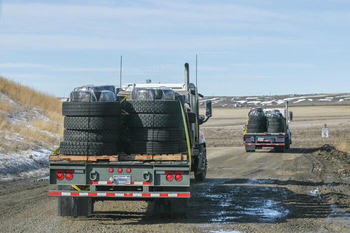 Rearview of two forty-foot tractor trucks loaded with pallets of tires driving.
