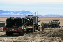 An airman in a high visibility vest walks around a forty-foot flatbed truck loaded with pallets of tires.