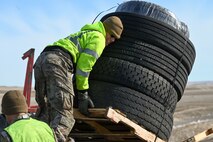 Airman in a highly visible vest unloads a pallet of tires