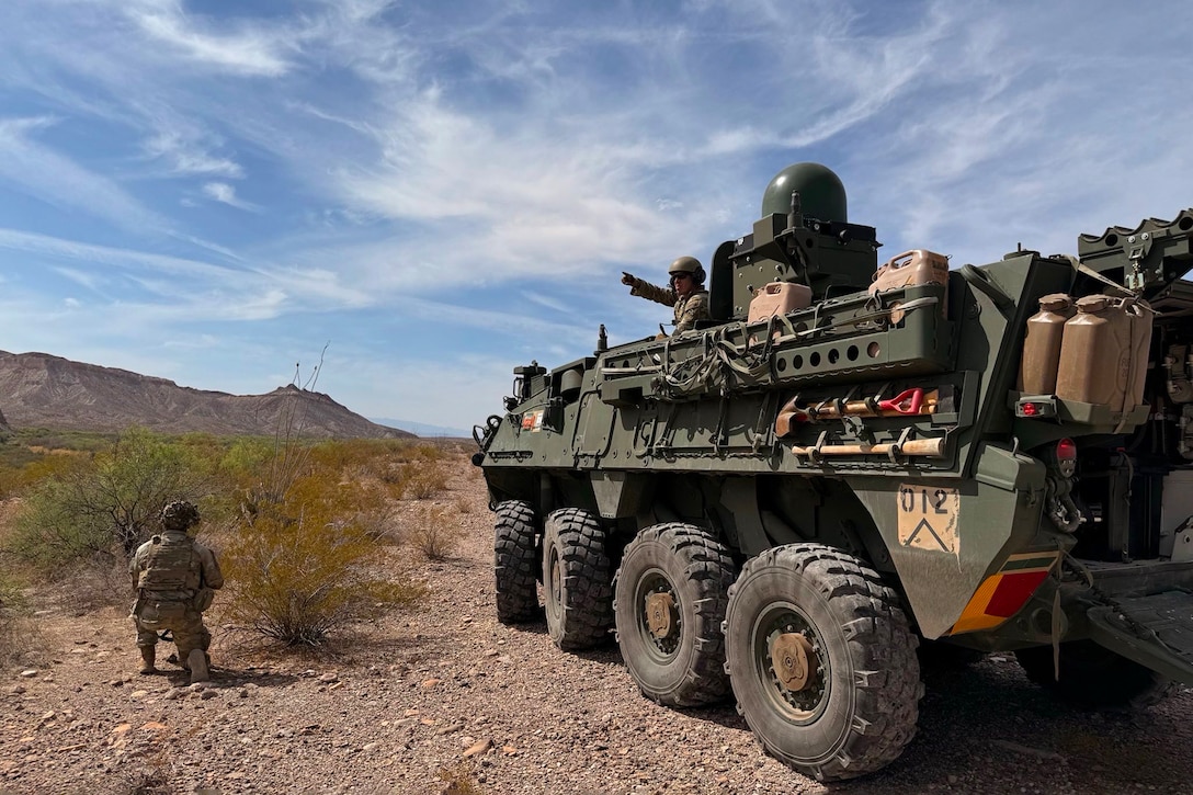 Soldiers in and next to an armored vehicle look out into a field.