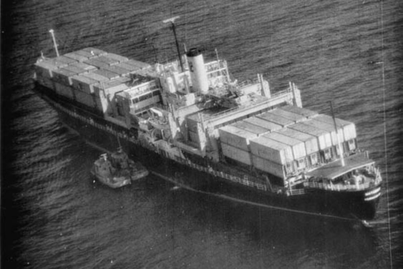 A container ship floats in the sea with two small boats beside it.