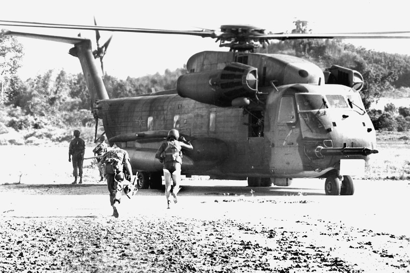 Four people run toward a helicopter.