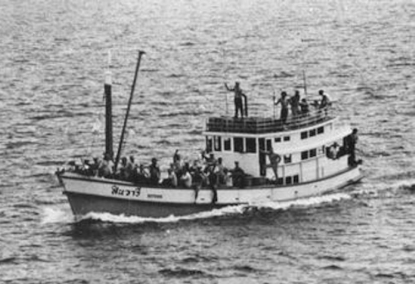 A small boat crowded with people floats at sea.